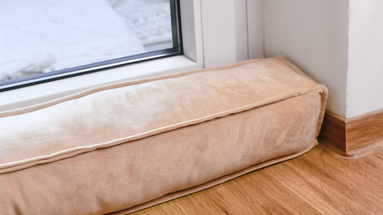 A thick pink cushion lying in front of a door to stop drafts