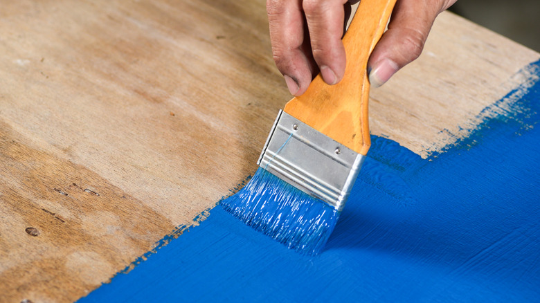 A hand painting a board a bright blue color