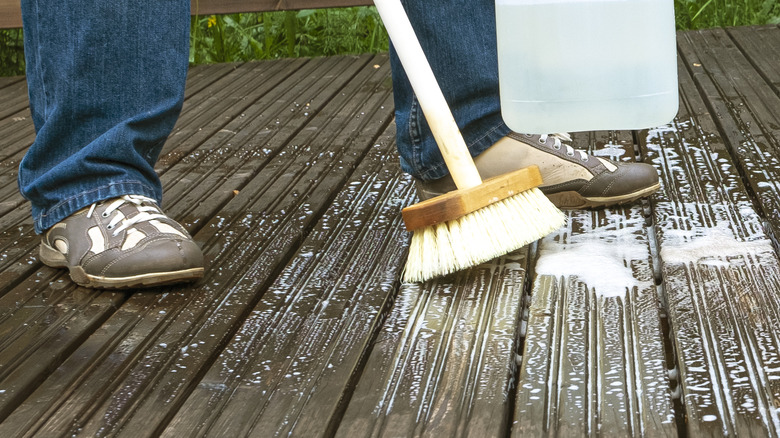 Man washes wood deck with scrub brush, soap, and vinegar