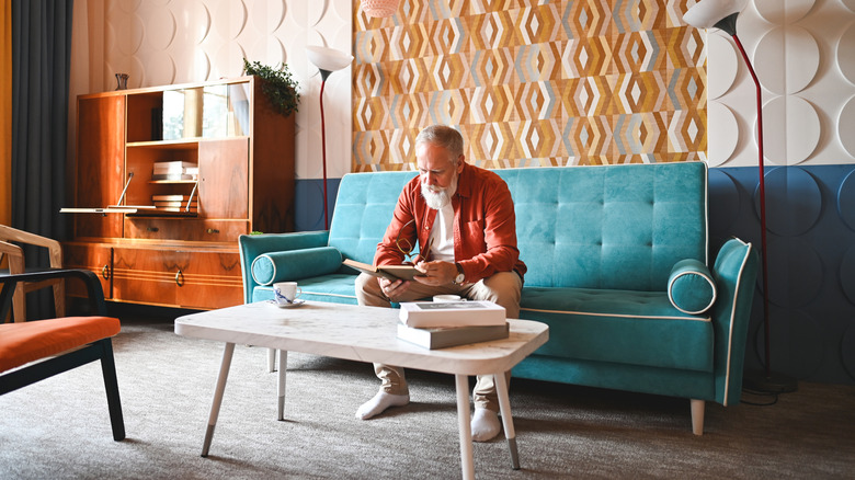 A man reads in a vintage-inspired living room with wall to wall carpet