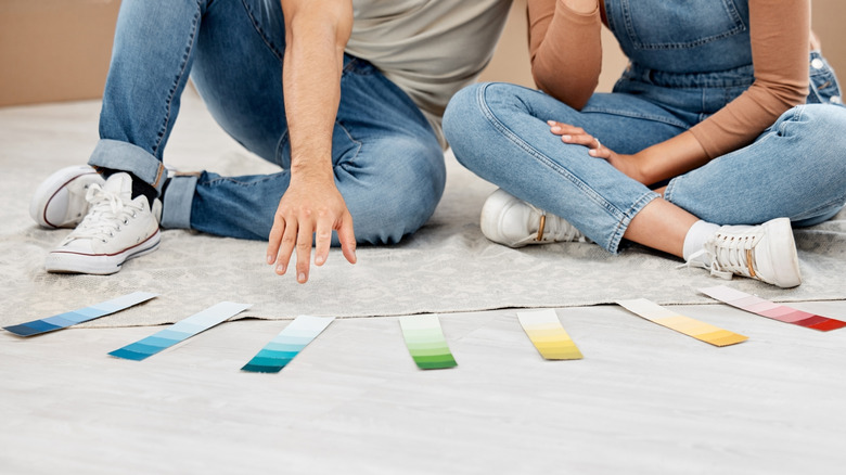 A couple sitting on the floor looking at paint color samples.