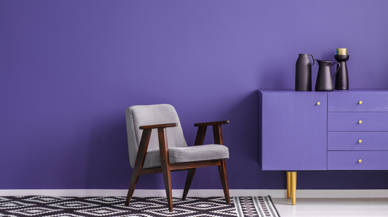 A contemporary room is decorated with purple walls, an armchair, and black home décor.