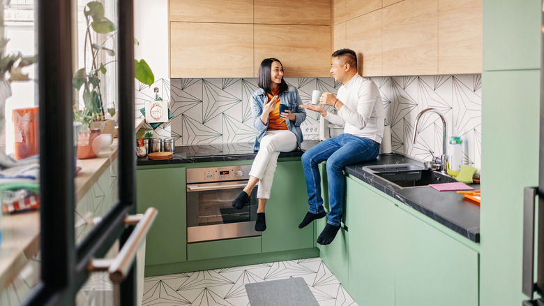 A couple sitting on the counters of a kitchen with wood cabinets and a striking backsplash.