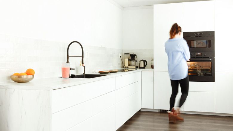 A woman standing in a monochromatic white kitchen.