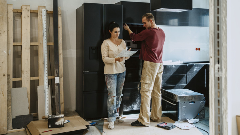 A couple standing in an unfinished kitchen with black cabinets