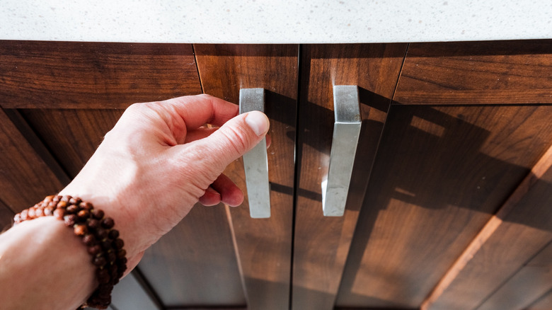 Person opening stained wood cabinets by handles