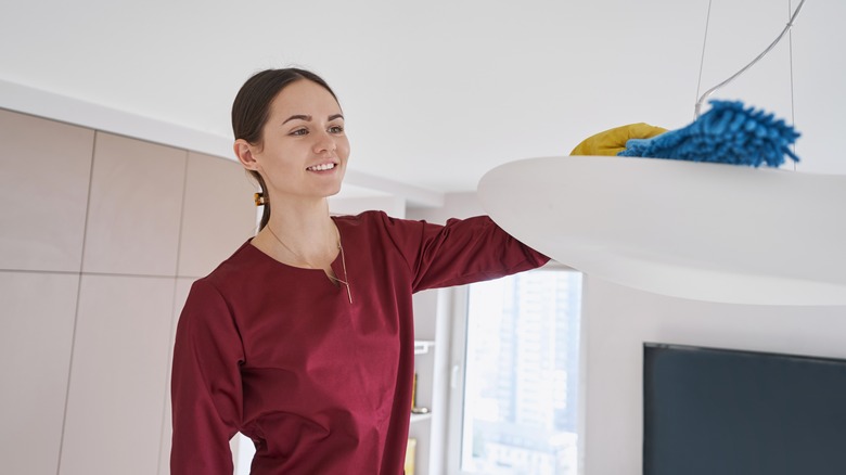 Woman dusting ceiling light fixture