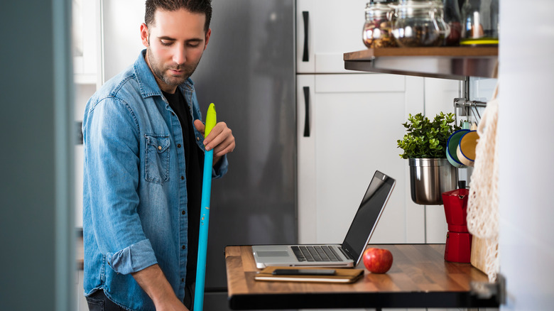 Man sweeping in kitchen by laptop