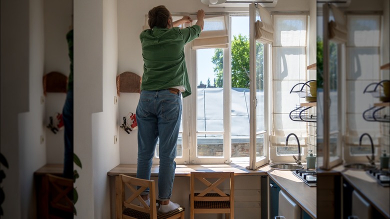 Man hanging blinds in kitchen