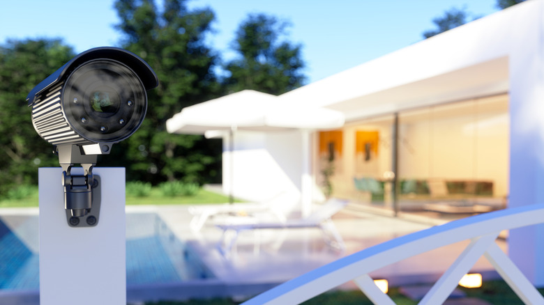 A mounted security camera sits in front of a home with a pool