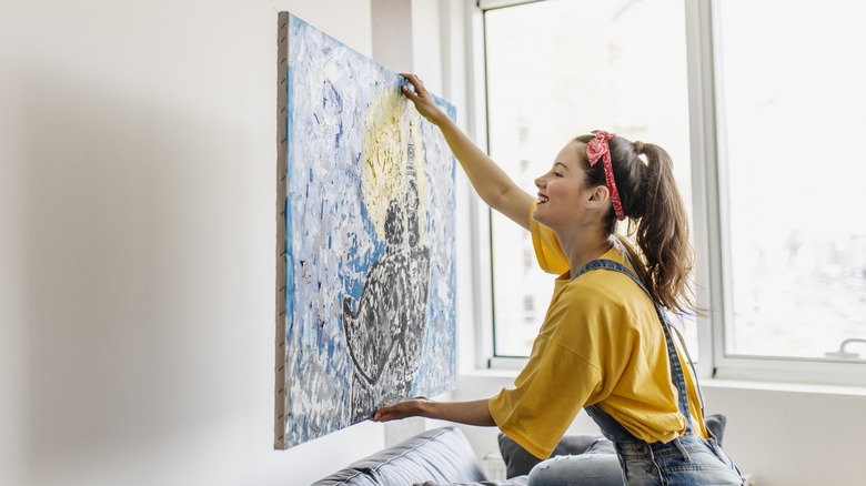 Woman hanging a large painting on an empty wall