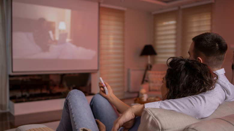 A couple watching a movie projected on a screen in their living room.