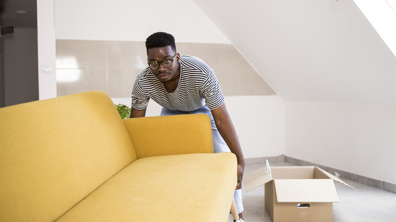 Man moving a yellow couch into an empty room.