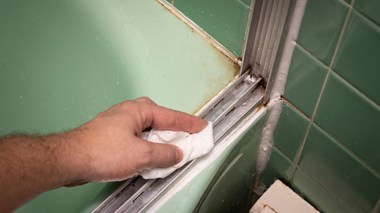 A person wiping down a shower door track