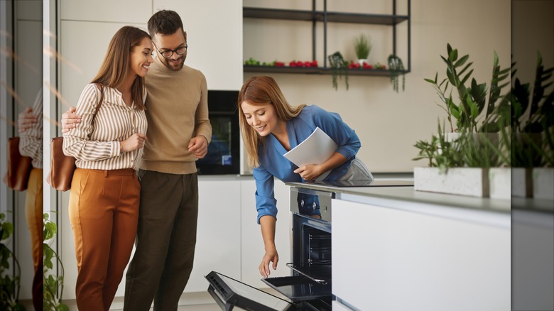 A real estate agent shows prospective homebuyers a dishwasher