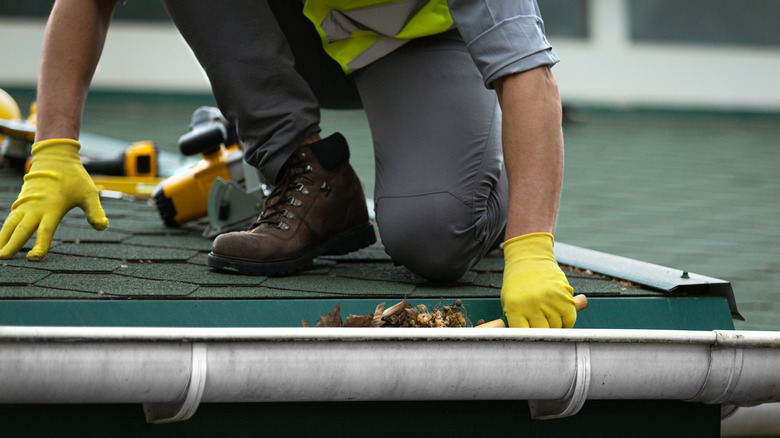 Man kneeling on roof cleaning gutters