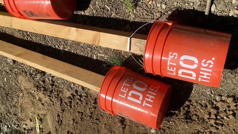 Fence poles set in orange 5 gallon buckets laying on ground