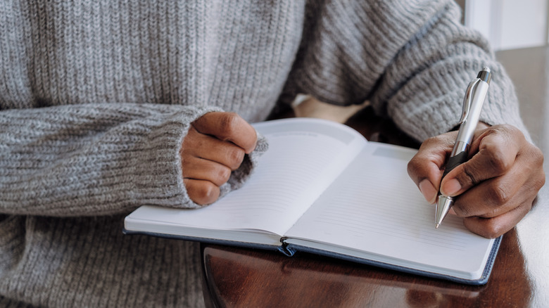 A person wearing a gray sweater jots down notes in a notebook.