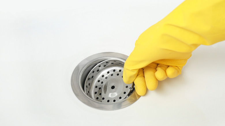 A person wearing gloves removes a strainer from a sink