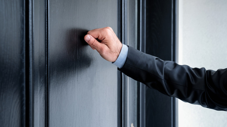 Person knocking on large, black front door
