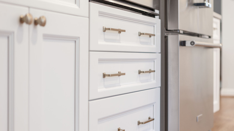 Close-up photo of white Shaker-style cabinets with brass knobs and handles.