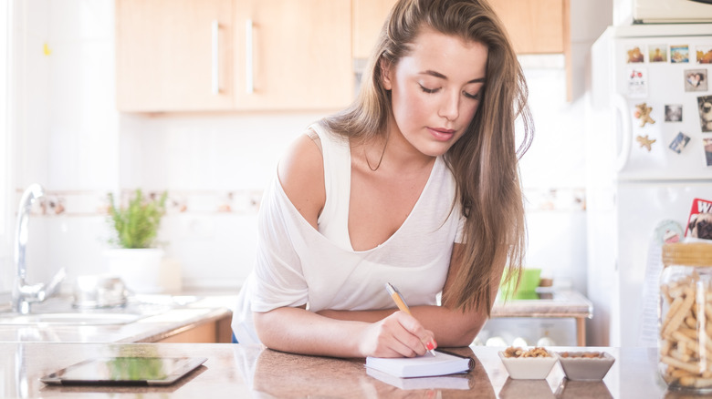 woman writing on paper on kitchen countertop