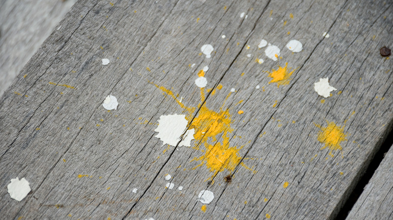 drops of dried white and yellow paint splatters on wooden floor