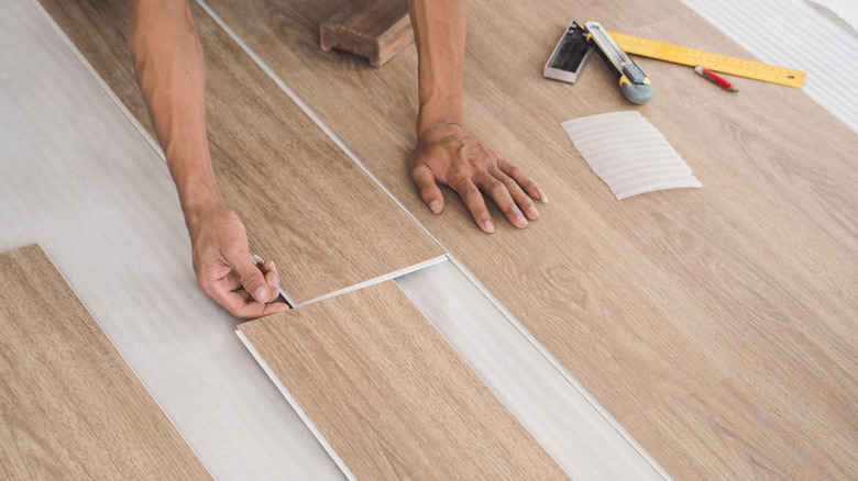 Two hands installing vinyl plank flooring.