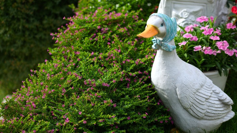 A goose statue standing in a garden near some shrubs.