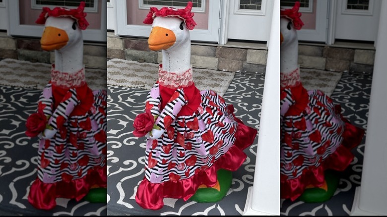 A concrete porch goose dressed up in a red outfit with hearts for Valentine's Day.