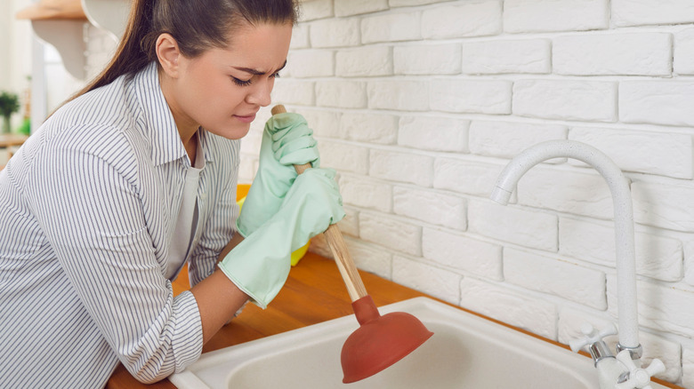 Woman trying to unblock a clogged drain in kitchen