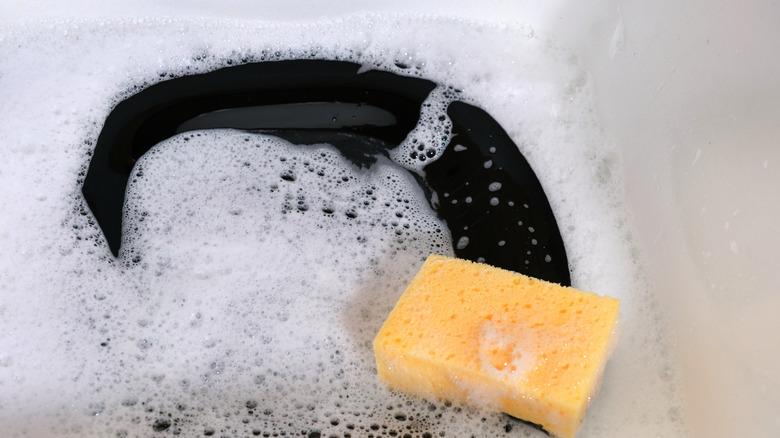 Black dish in soapy sink with sponge