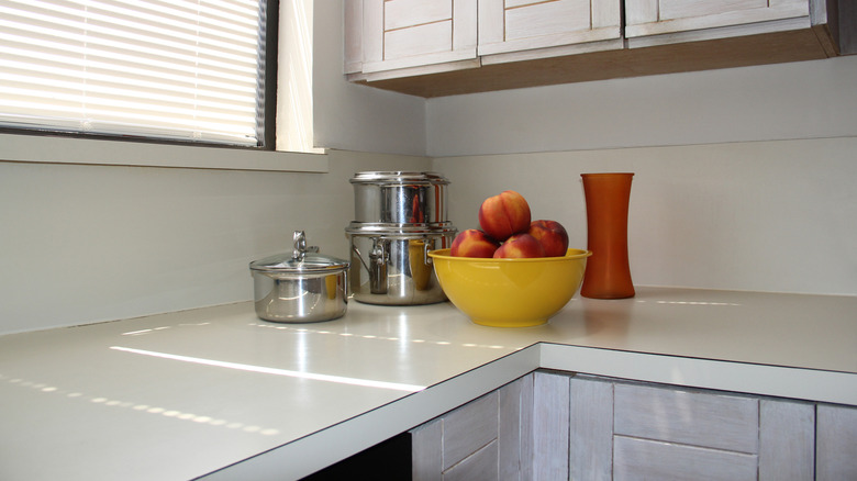 A white laminate countertop with a bowl of fruit, pots, and a vase