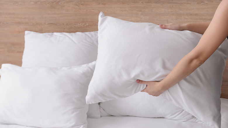 Person fluffing white bed pillow