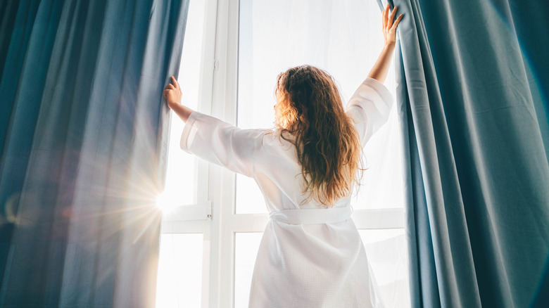 Woman opening bedroom curtains