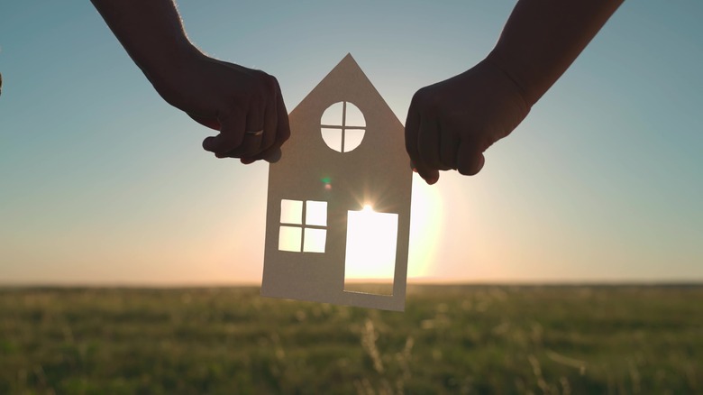 holding paper house against sunset