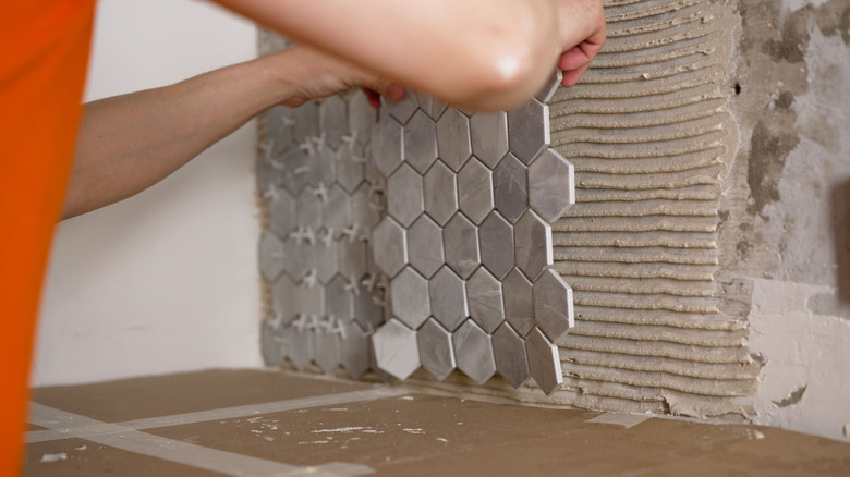 Person holding kitchen backsplash tiles in front of wall