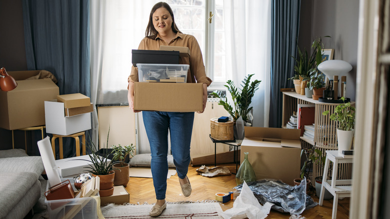 Woman walking through messy living room with boxes of items