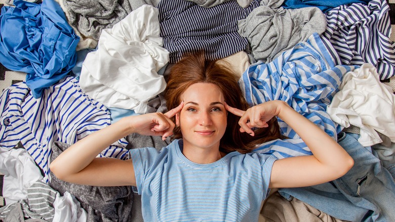 Pensive woman laying in a clothing pile