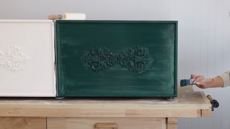 Woman applying green paint to white IKEA storage unit with trim and applique additions