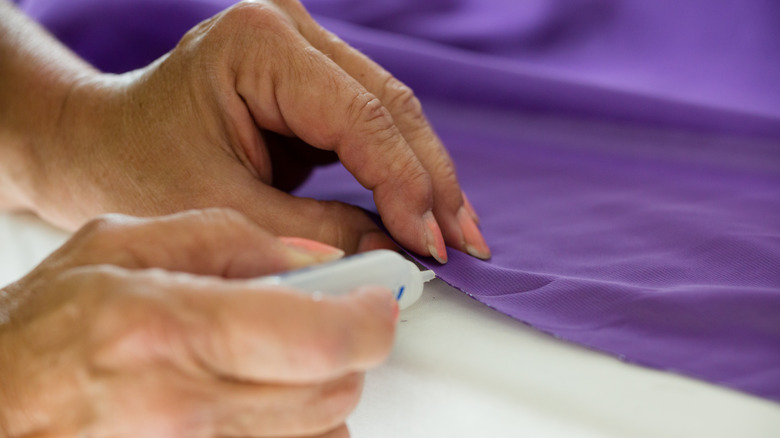 Hands applying glue to purple fabric