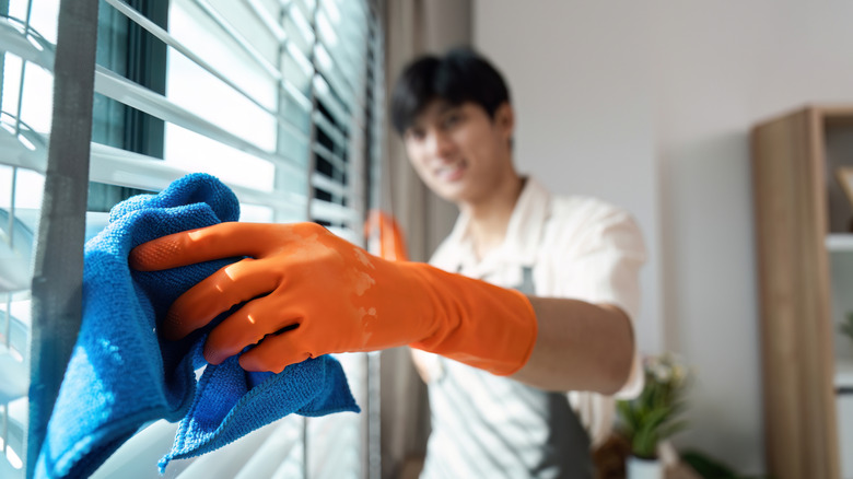 Man cleaning window blinds with cloth