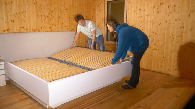 A man and woman insert bunkie boards into a white bed frame