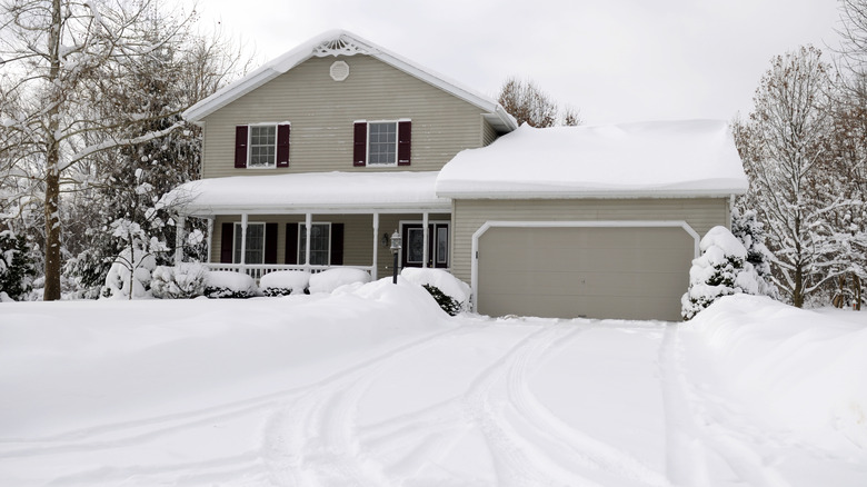 Snow covers the lawn and driveway in front of a house