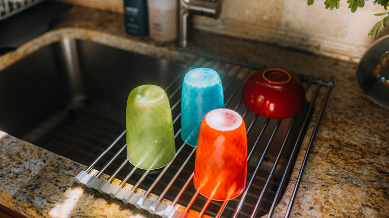 A dish sits rack over a sink with freshly washed cups drying on it.