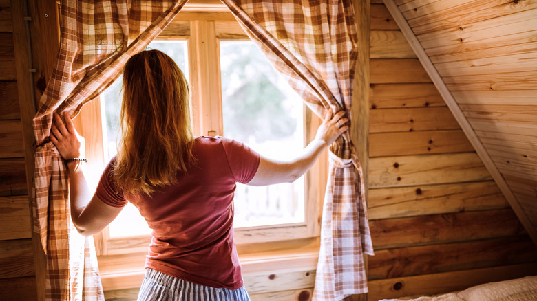 A woman opening curtains in cabin