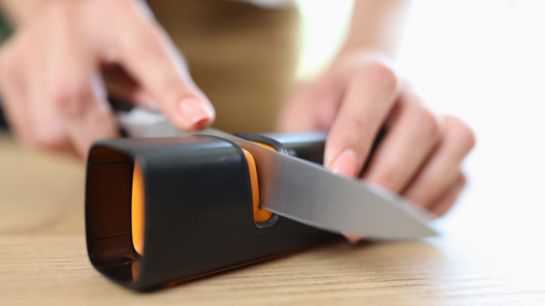 A person sharpens their kitchen knife with a special tool