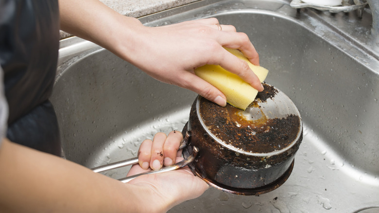 Person scrubbing a burned pot in a sink