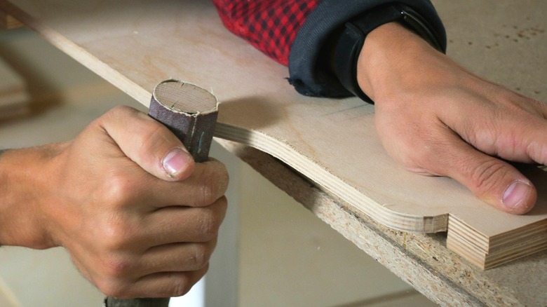 person sanding rounded plywood edge