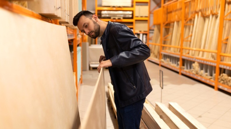 man in leather jacket checking edge of plywood sheet in home improvement center